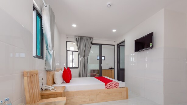 Habitación de hotel moderna con una cama de madera, una mesa de vidrio y un televisor montado en la pared.