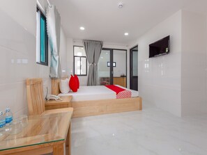 Habitación de hotel moderna con una cama de madera, una mesa de vidrio y un televisor montado en la pared.
