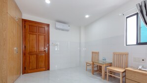 Una habitación limpia y moderna con un armario de madera, una pequeña mesa con sillas, un escritorio con teléfono y un equipo de aire acondicionado en la pared.