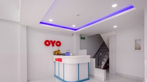 Un área de recepción con un mostrador blanco, un logotipo rojo y una escalera que sube a un piso superior.