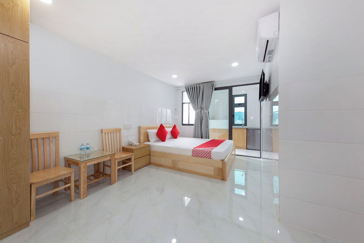 A modern hotel room with a bed, wooden furniture, a small table, and a glass partition.