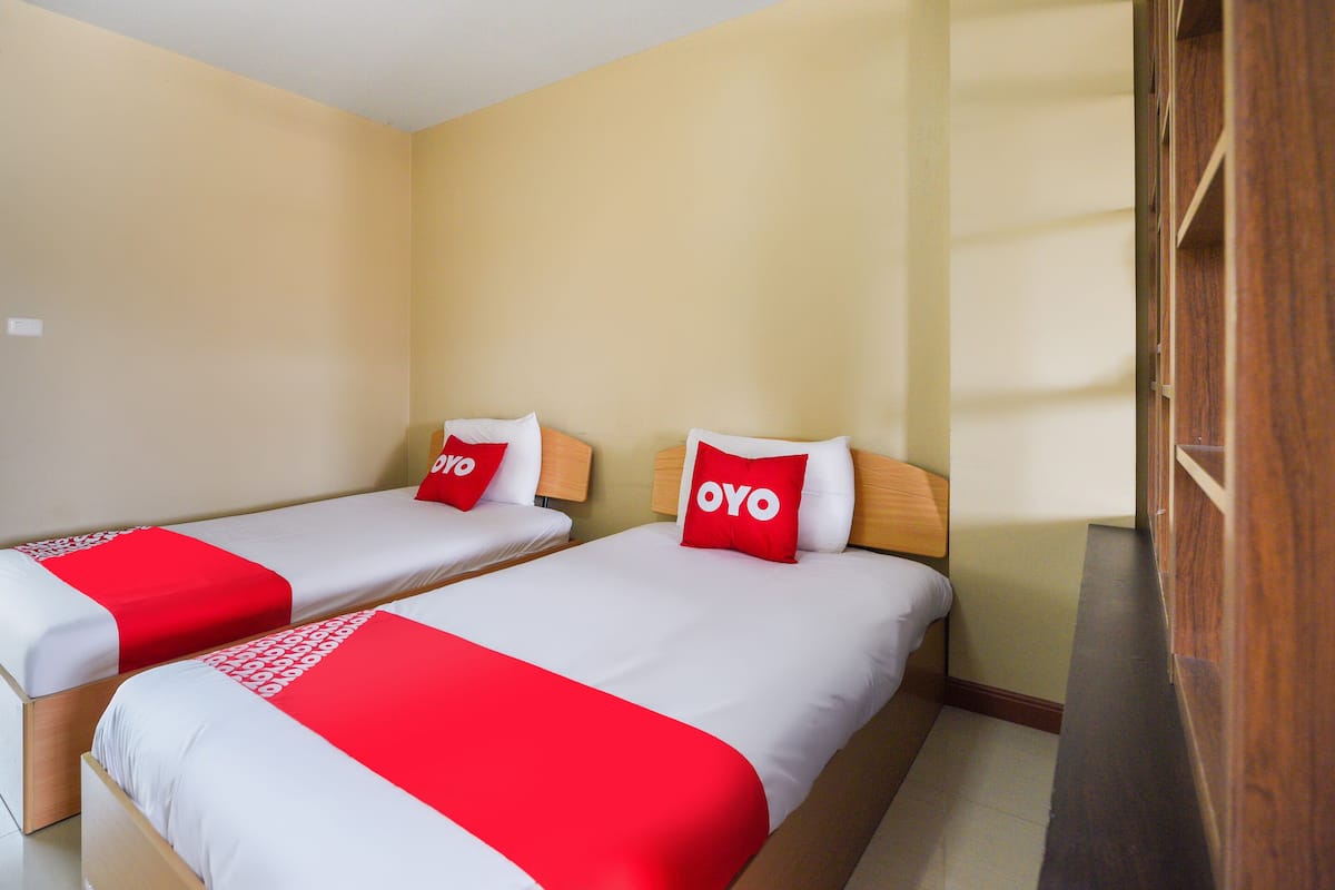 A hotel room with two single beds, each with a red and white bedspread and a pillow labeled "OYO".