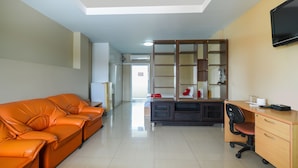 A room with a sofa, a desk, a chair, a TV, and a wardrobe. - OYO 762 Chompoo (Nakhon Chai Si)