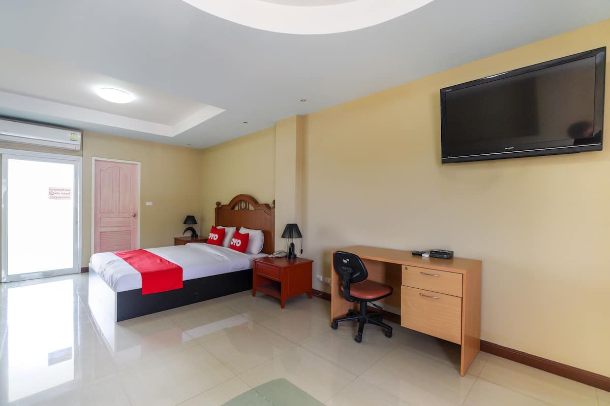A hotel room with a bed, desk, chair, TV, and a door.