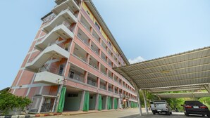A multi-story hotel with balconies, a covered parking area, and a green awning. - OYO 762 Chompoo (Nakhon Chai Si)