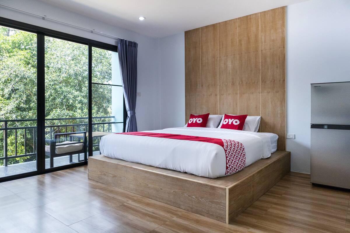 Une chambre moderne avec un grand lit, une tête de lit en bois et un balcon avec une porte vitrée.
