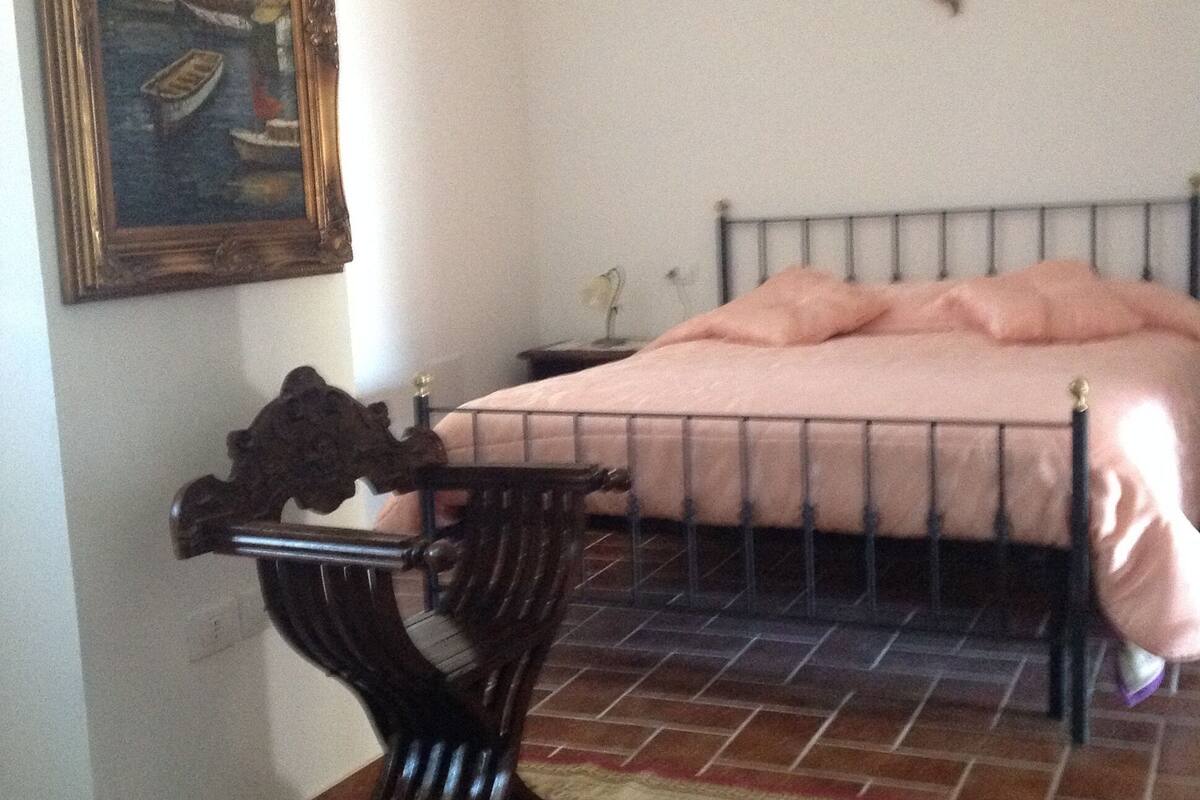A bedroom with a bed, a nightstand, a chair, a rug, and a painting on the wall.