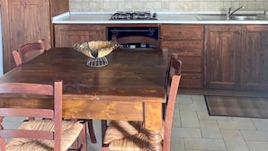 A kitchen with wooden cabinets, a tiled backsplash, a gas stove, and a dining table with chairs. - Agriturismo Casanova (Gubbio)
