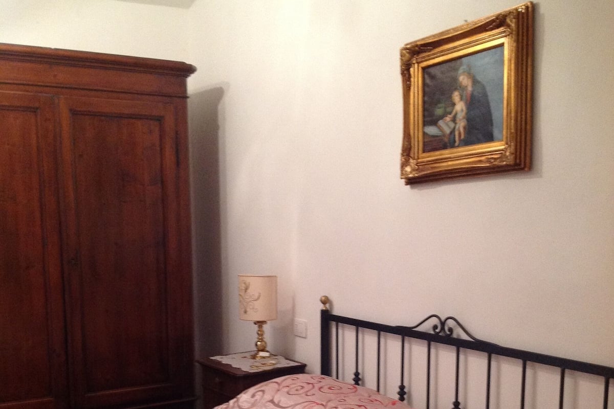 A bedroom with a bed, a wooden wardrobe, a nightstand with a lamp, and a framed picture on the wall.