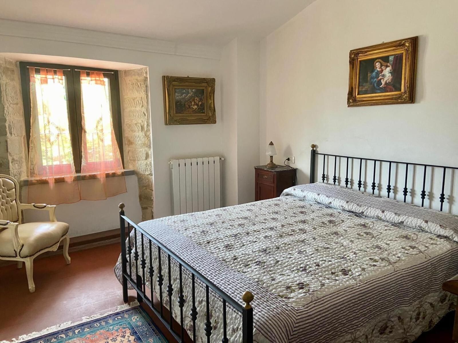 A bedroom with a bed, a chair, a radiator, and two framed pictures on the wall.