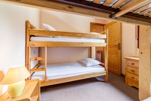 A bunk bed with a wooden frame, a single bed below, and a small bedside table with a lamp. - Homerez - Apartment in Bolquère, mountain view (Bolquère)