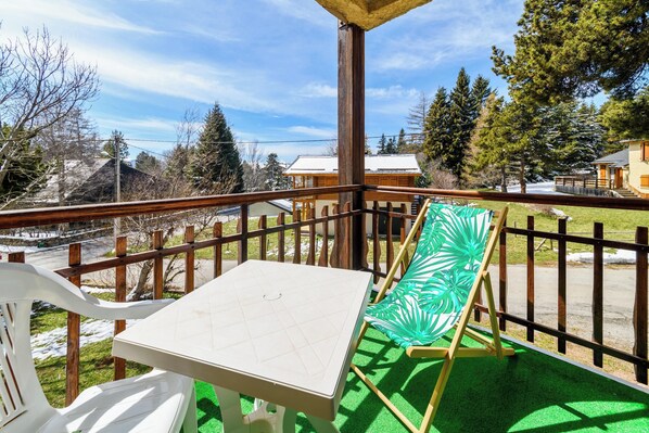 A balcony with a table and chairs, a view of trees and buildings, and a wooden railing. - Homerez - Apartment in Bolquère, mountain view (Bolquère)