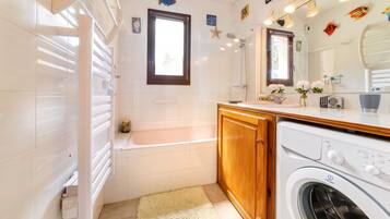 A modern bathroom with a bathtub, a washing machine, and a large mirror.