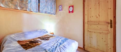 A bedroom with a bed, a wooden door, and a wall with a curtain.