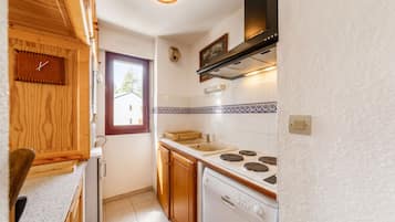 Une cuisine de taille réduite, dotée de meubles en bois, d’une cuisinière blanche et d’une fenêtre laissant entrer la lumière naturelle.