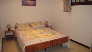 Een slaapkamer met een houten bed, twee nachtkastjes met lampen, een aan de muur hangend schilderij en een raam met een bloemenprint gordijn.