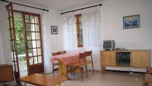 Een kamer met een eettafel, stoelen, een televisie en een kast.