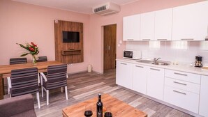 A modern kitchen with white cabinets, a microwave, and a sink. There is a dining area with striped chairs and a wooden table. - Villa Angy (Plitvicka Jezera)