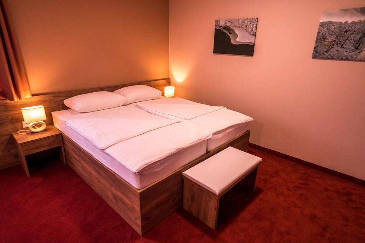 A neatly made bed with a wooden headboard, a bedside table with a lamp, and a small bedside table with a telephone.