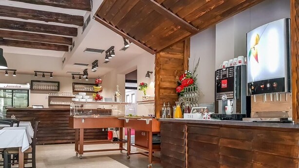 A restaurant interior with wooden beams, a counter with a coffee machine, and a display case. - Villa Angy (Plitvicka Jezera)