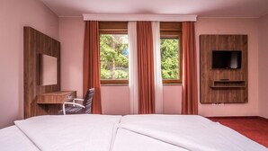 A hotel room with a large bed, a desk, a chair, a TV mounted on the wall, and a window with curtains. - Villa Angy (Plitvicka Jezera)