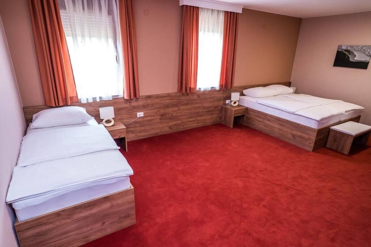 A hotel room with two beds, wooden headboard, red carpet, and a painting on the wall.