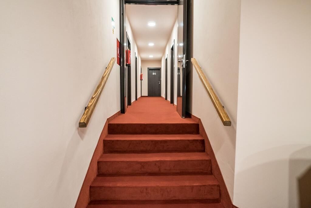 Un pasillo de hotel con una escalera alfombrada de color rojo, barandillas de madera y una puerta al final.
