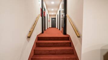 A hotel hallway with a red carpeted staircase, wooden handrails, and a door at the end.