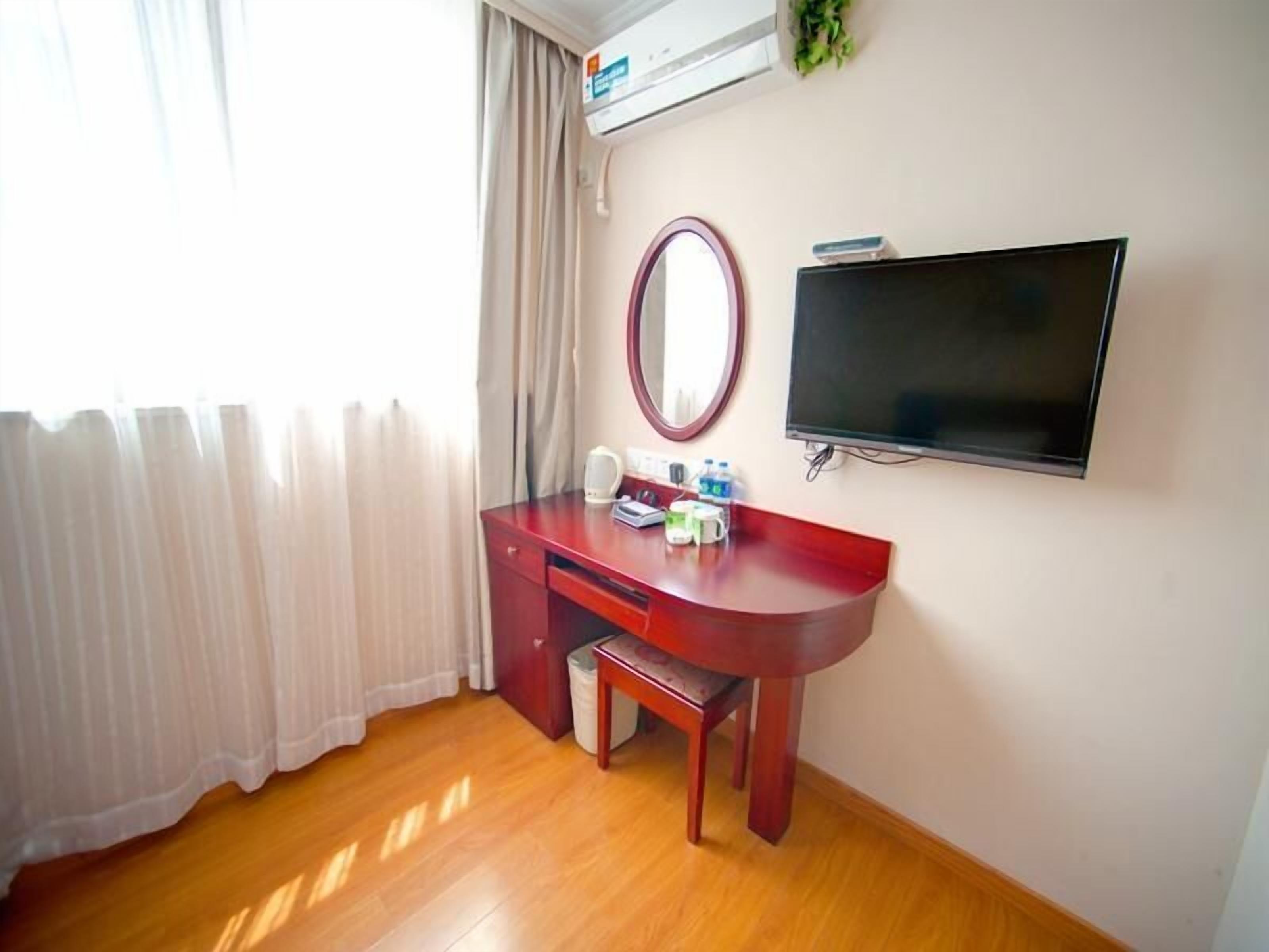 A hotel room with a wooden desk, a mirror, a flat-screen TV, and a window with curtains.
