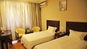 A hotel room with two single beds, a desk with a chair, a small table with a lamp, and a window with curtains.