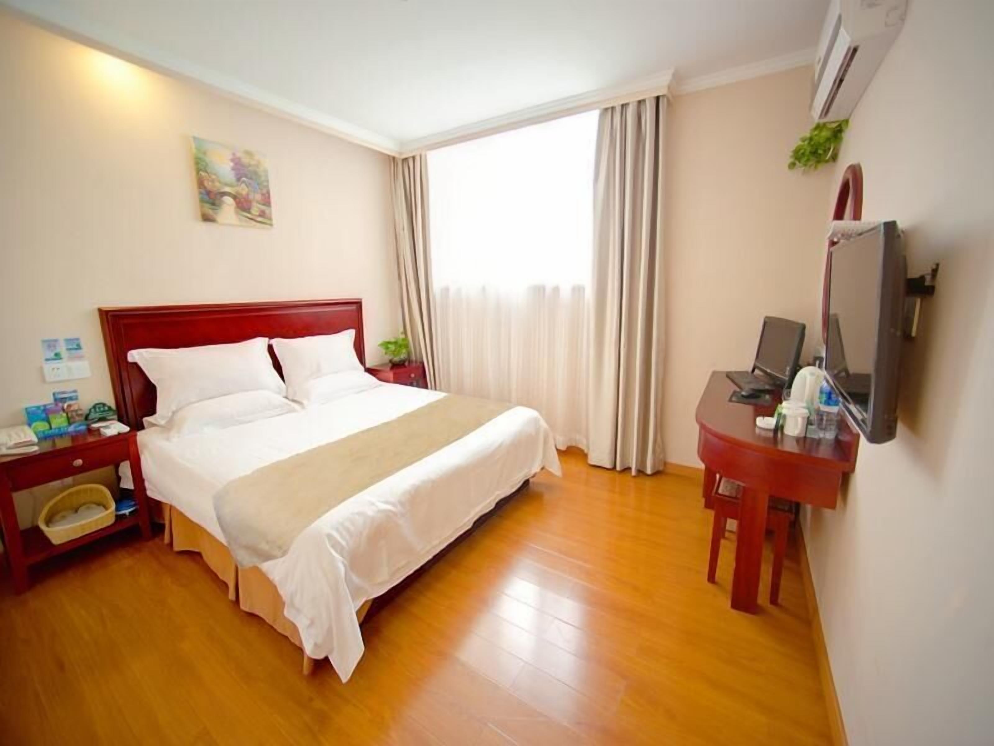 A hotel room with a wooden floor, a bed with white linens, a desk with a computer, and a TV on the wall.