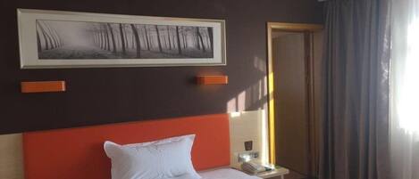 A hotel room with a large bed, a framed picture on the wall, a nightstand, and a door with curtains.