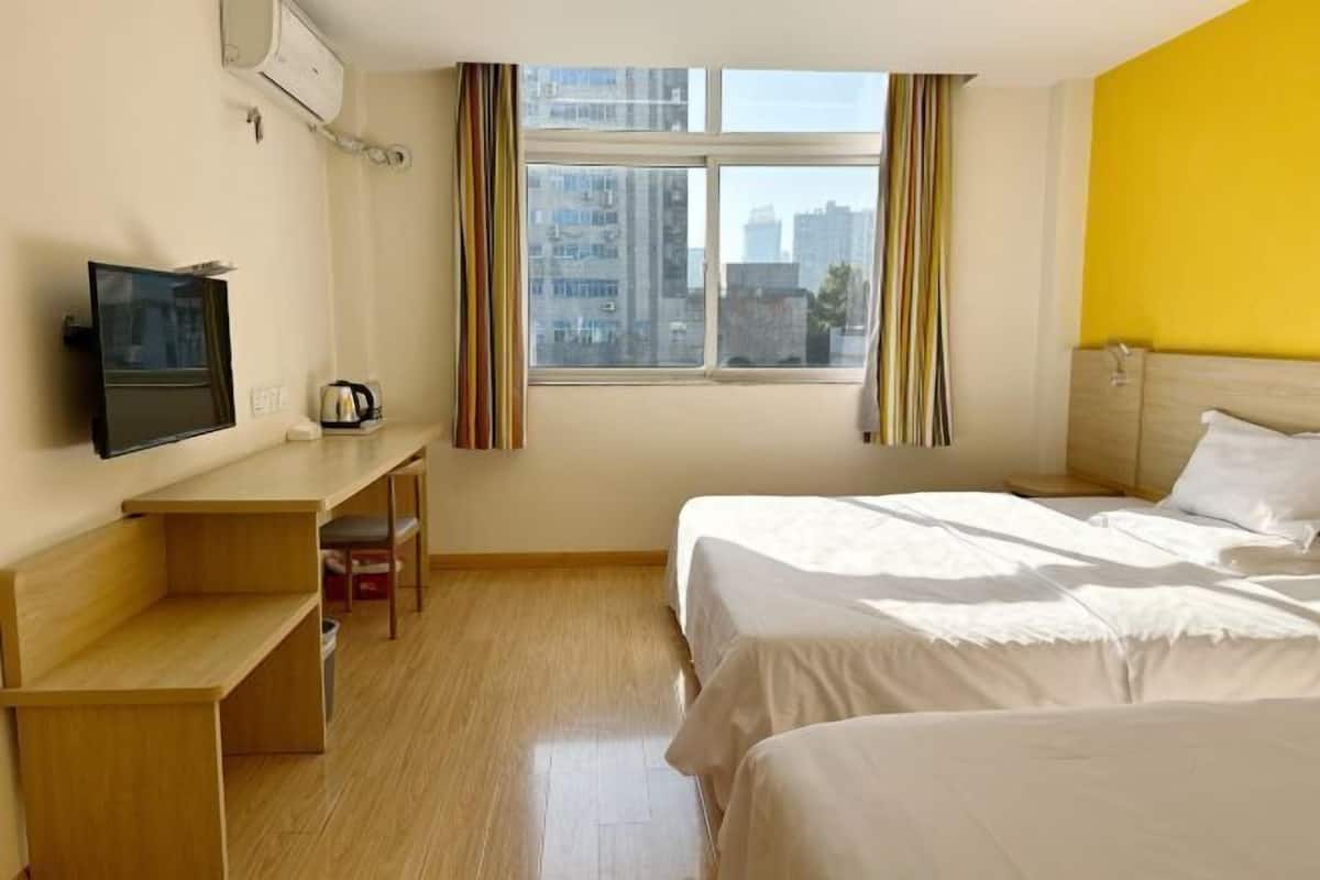 Una habitació d'hotel amb llit, escriptori, cadira, televisió i finestra amb cortines.