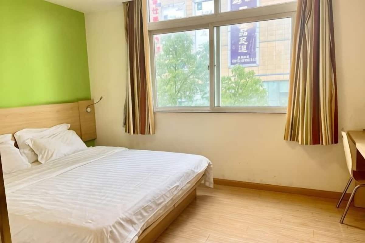A hotel room with a bed, a window with curtains, a desk, and a chair.