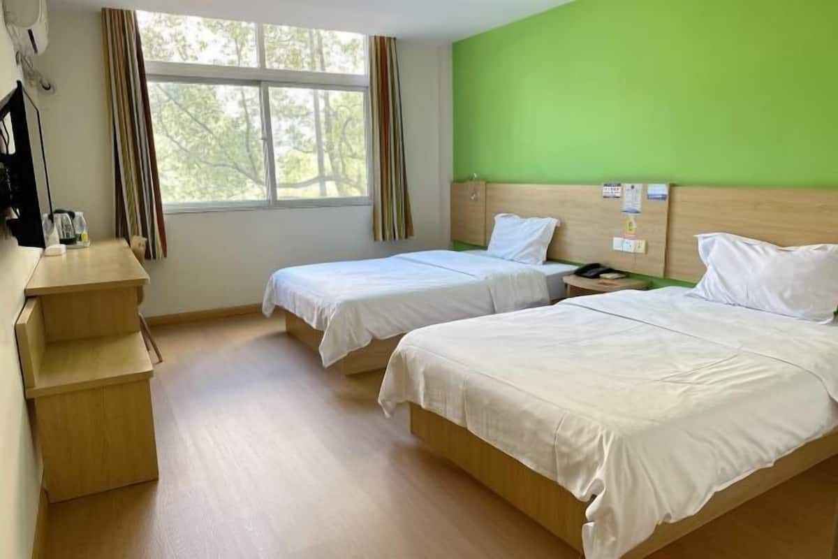 Habitació amb dos llits, un escriptori, una finestra amb cortines i una paret verda.