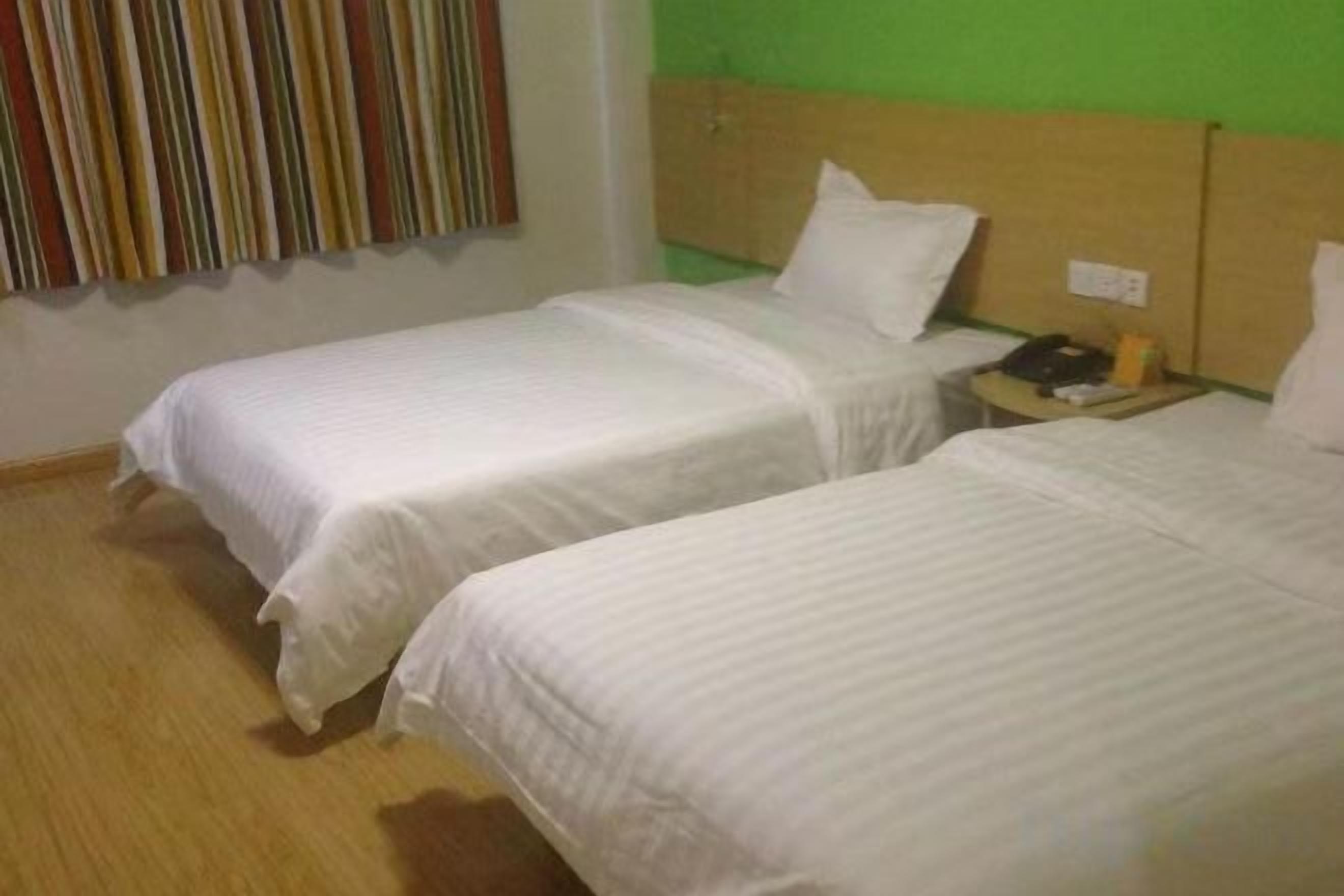 A hotel room with two single beds, a wooden headboard, a nightstand with a lamp, and a striped curtain.