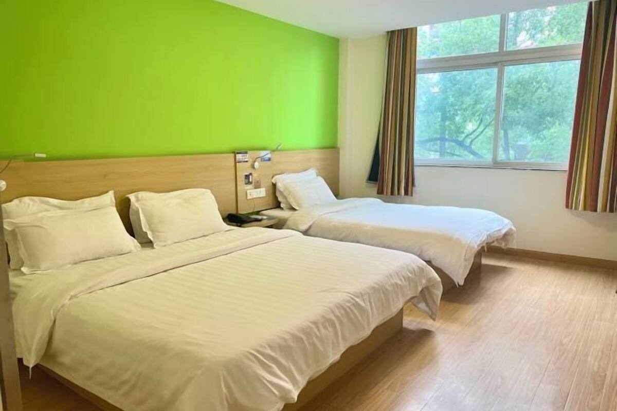 Habitació d'hotel amb dos llits, una paret verda, una finestra amb cortines i un terra de fusta.