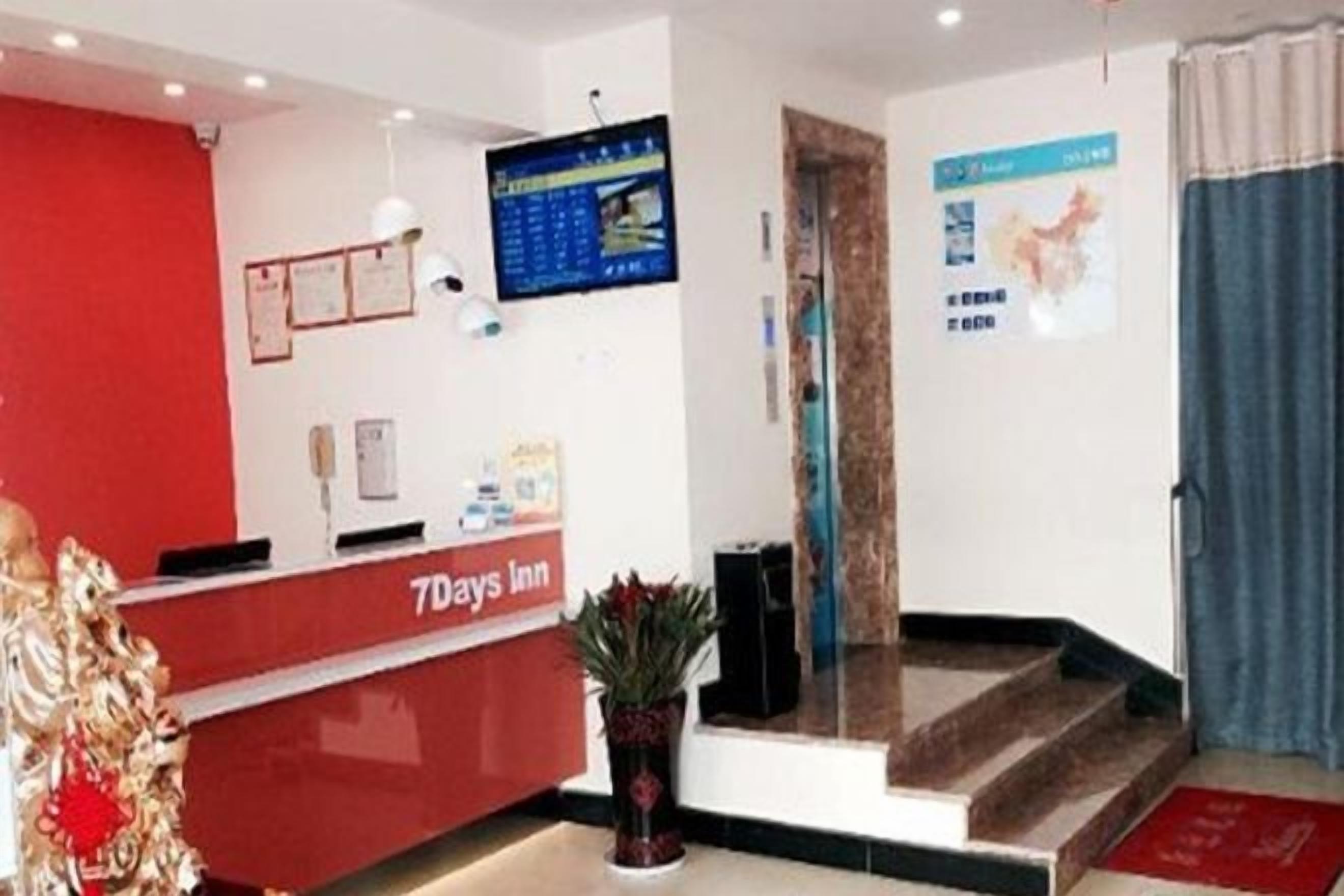 A reception area with a red desk, a digital screen, and a staircase leading to an upper floor.