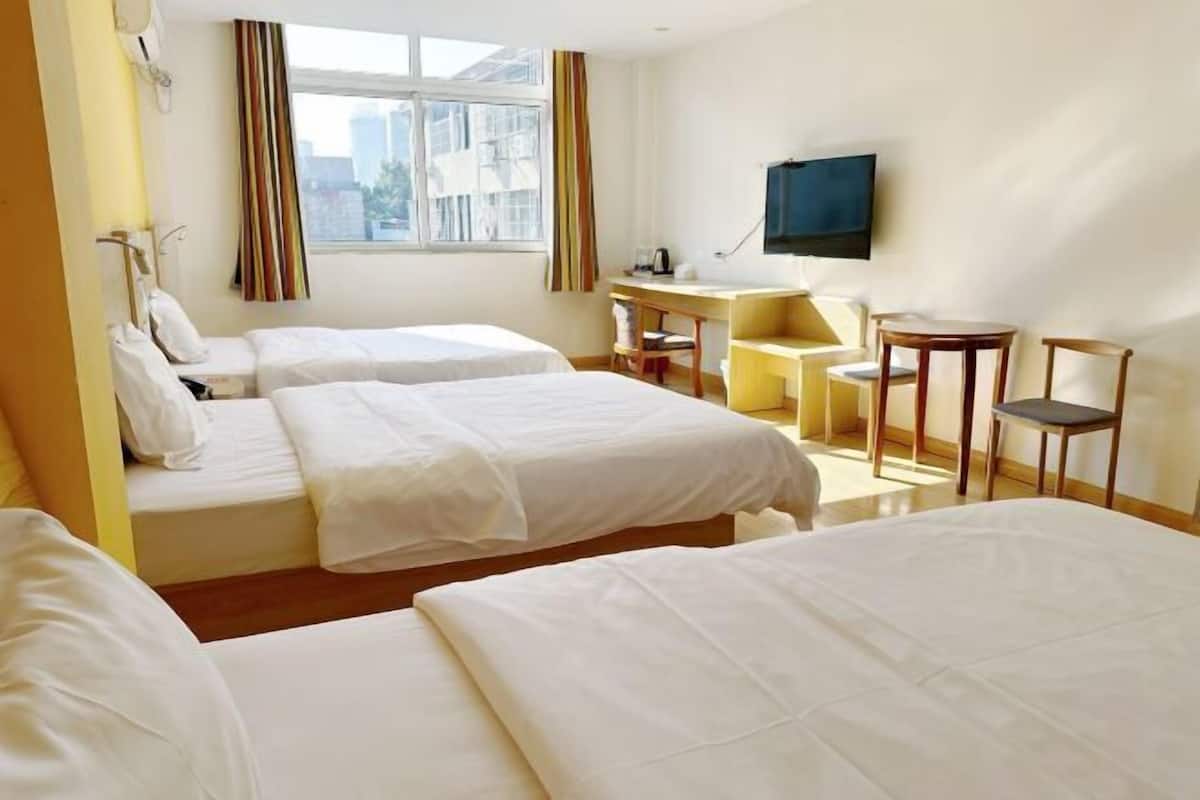 Habitació d'hotel amb dos llits, una taula de treball, una cadira, un televisor i una finestra amb cortines.