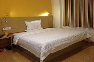 Una cama individual con cabecera de madera, una mesita de noche con lámpara y una pared con rayas verticales.