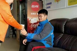 A person seated on a leather couch with a Coca-Cola advertisement in the background.