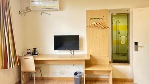 A modern room with a wooden desk, a television, a shower area, and a hanging clothes rack.