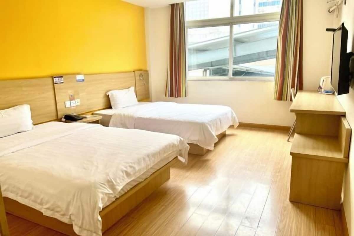 Habitació d'hotel amb dos llits, terres de fusta, una finestra amb cortines i un escriptori amb una cadira.