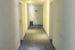 Un couloir étroit au revêtement de sol à motifs, une porte sur la gauche et une enseigne au-dessus de la porte.