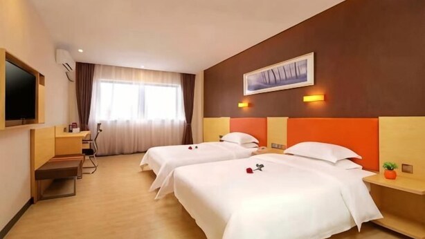 A hotel room with two beds, a desk, a TV, and a window with curtains.