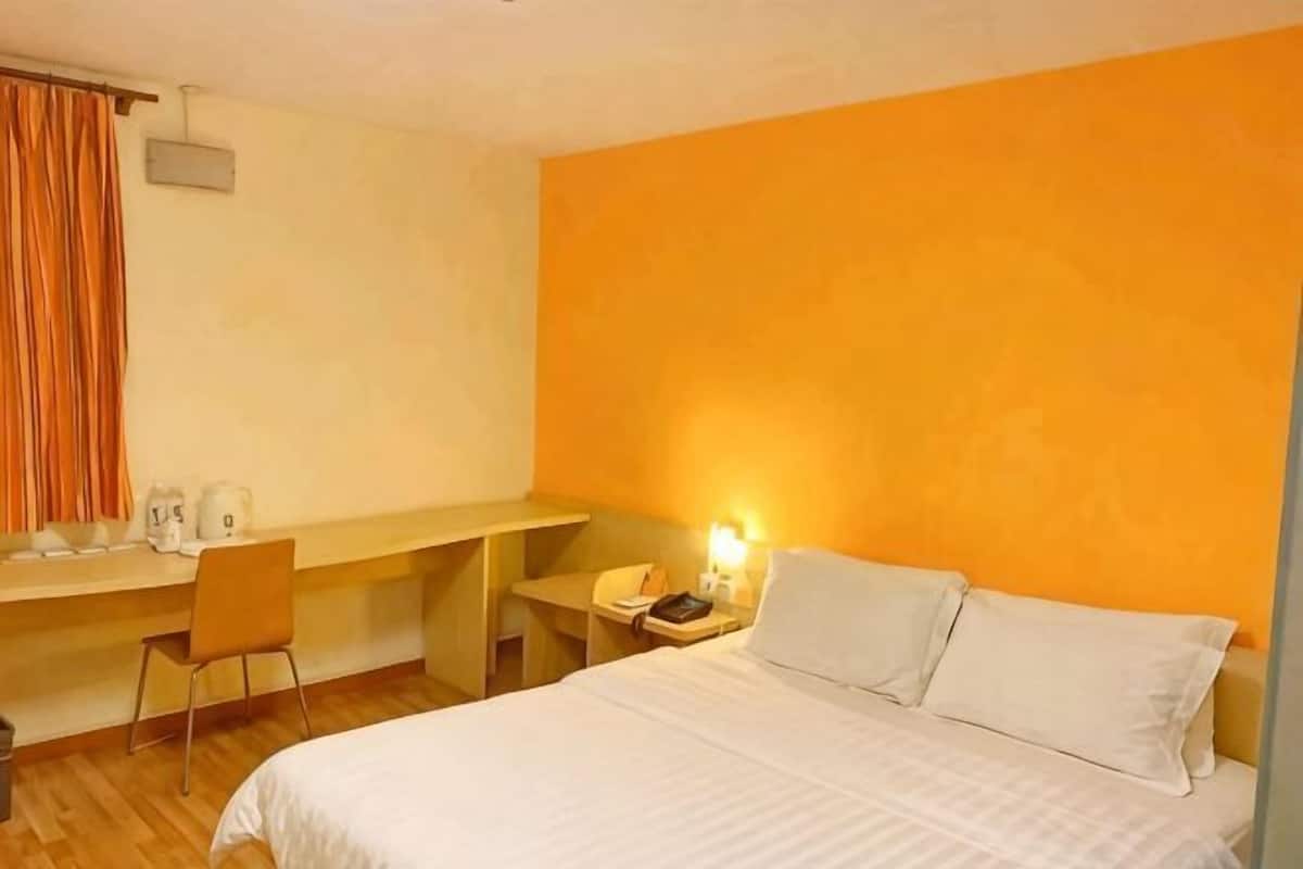 Habitació d'hotel amb llit, escriptori, cadira i tauleta de nit amb làmpada.