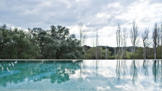 A clear swimming pool with a tiled bottom, surrounded by trees and a cloudy sky. - Herdade do Barrocal de Baixo (Montemor-o-Novo)
