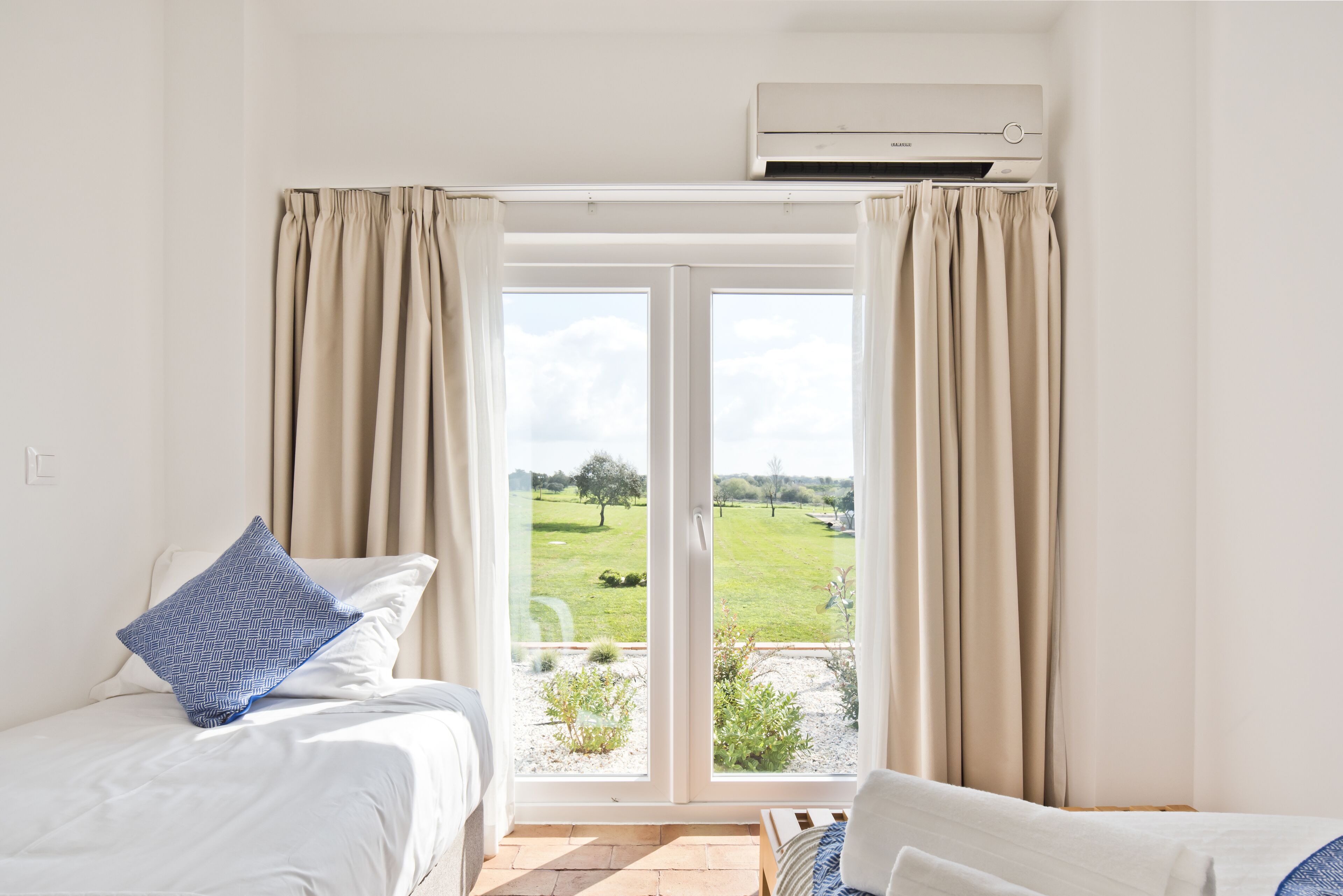 A bedroom with two beds, a large sliding glass door to a garden, and an air conditioning unit above the door.