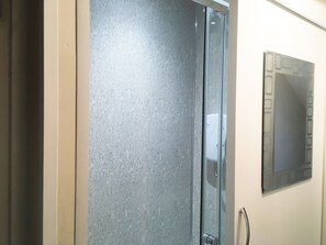 A bathroom with a glass shower enclosure and a wall-mounted control panel.