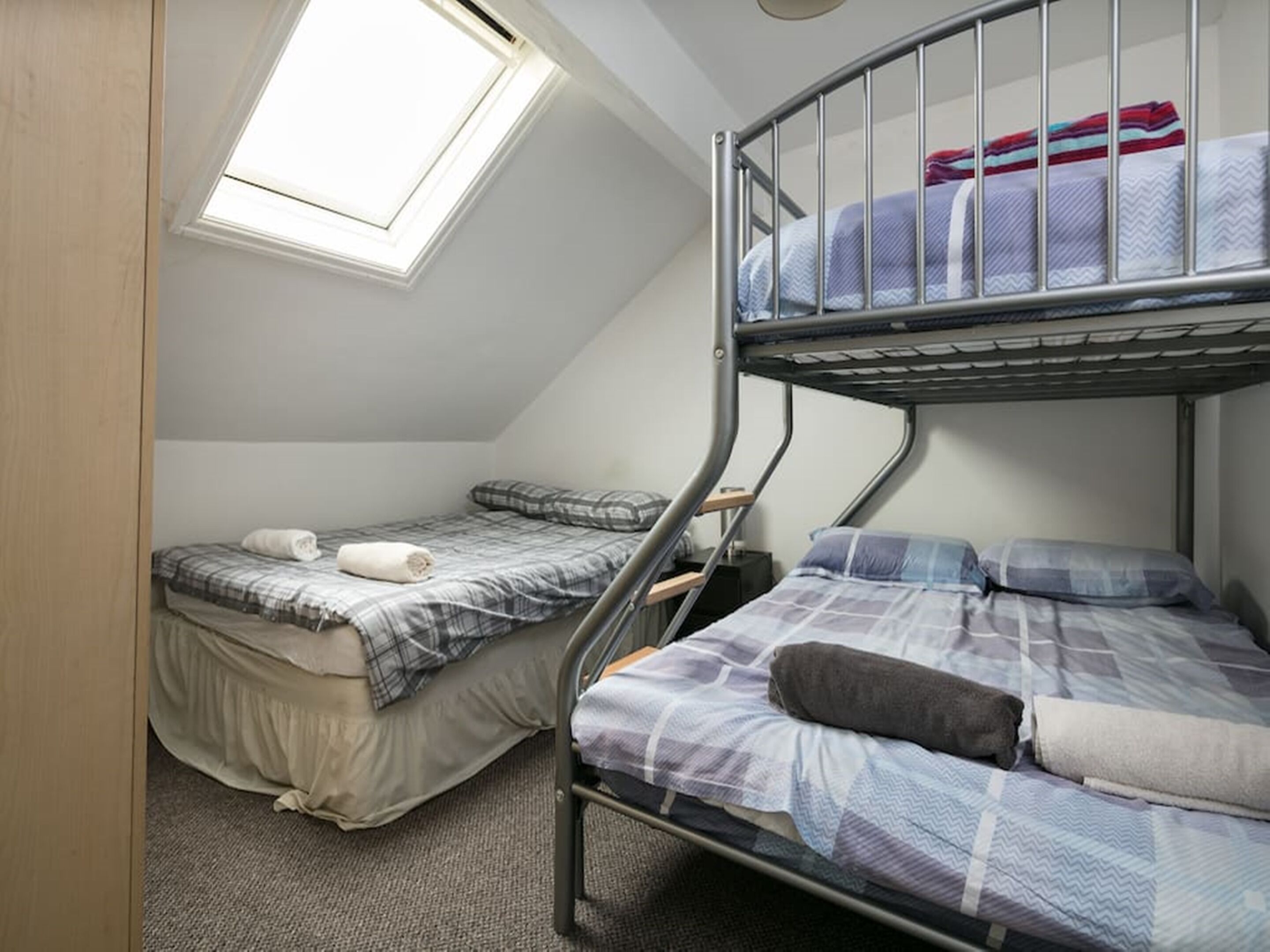 A dormitory room with bunk beds, a skylight, and a small desk.